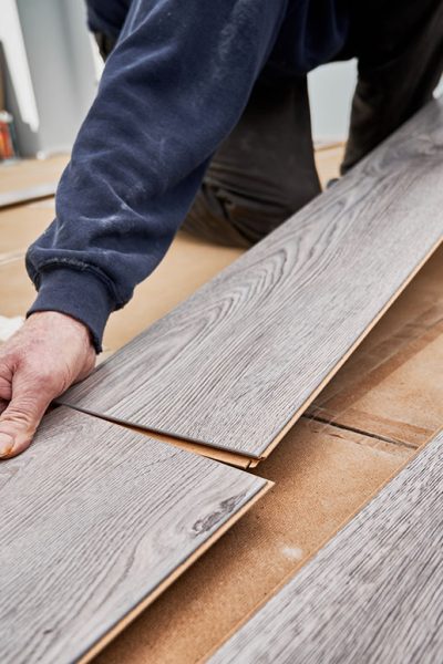 Close up of man hands laying laminate wooden planks on the floor in apartment under renovation. Male construction worker installing timber laminate flooring at home. Hardwood floor renovation concept.